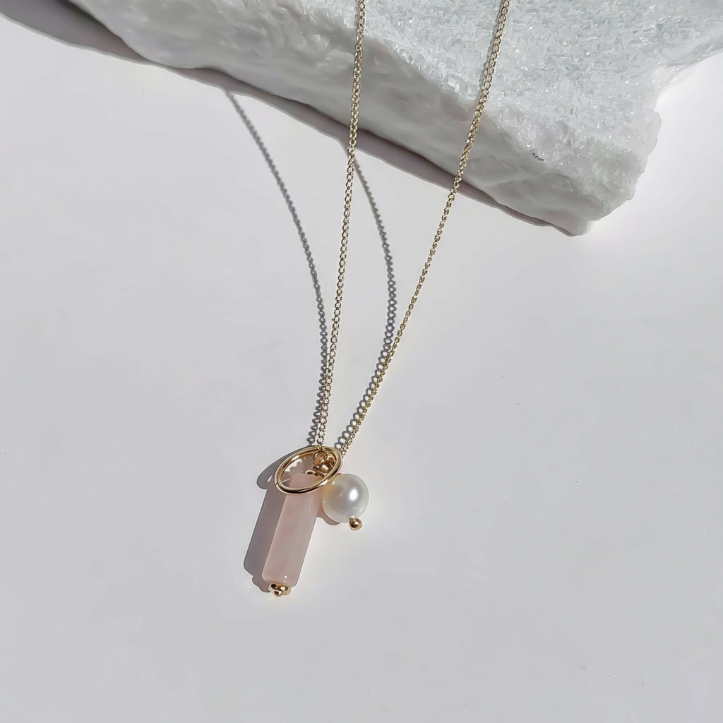 A rose quartz cluster necklace with gold circle charm and freshwater pearl on a fine gold chain, displayed against a white background.